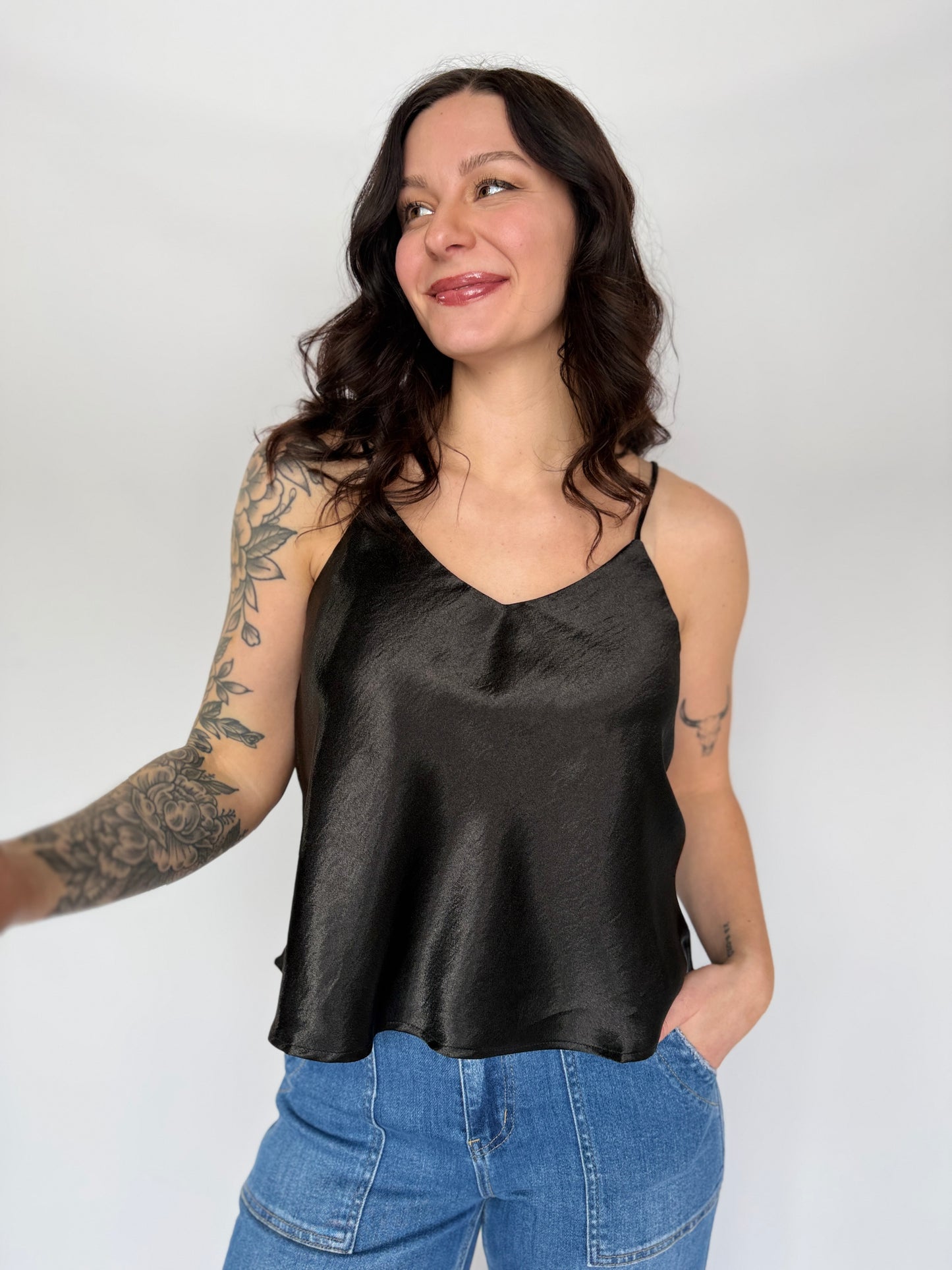 Woman wearing a black satin tank top and blue jeans against a white background
