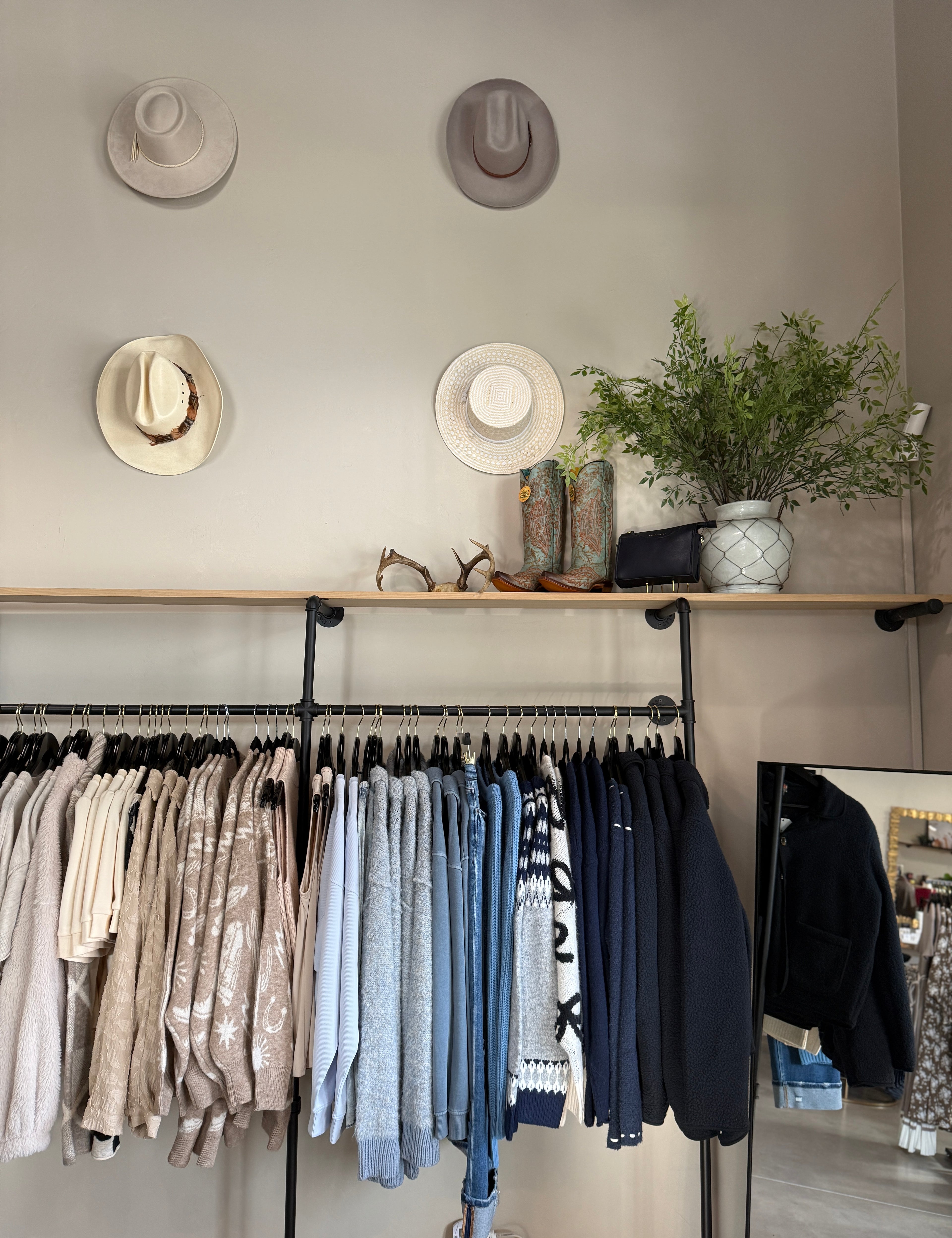 Clothing rack with shirts and pants, hats on the wall, and decorative items.