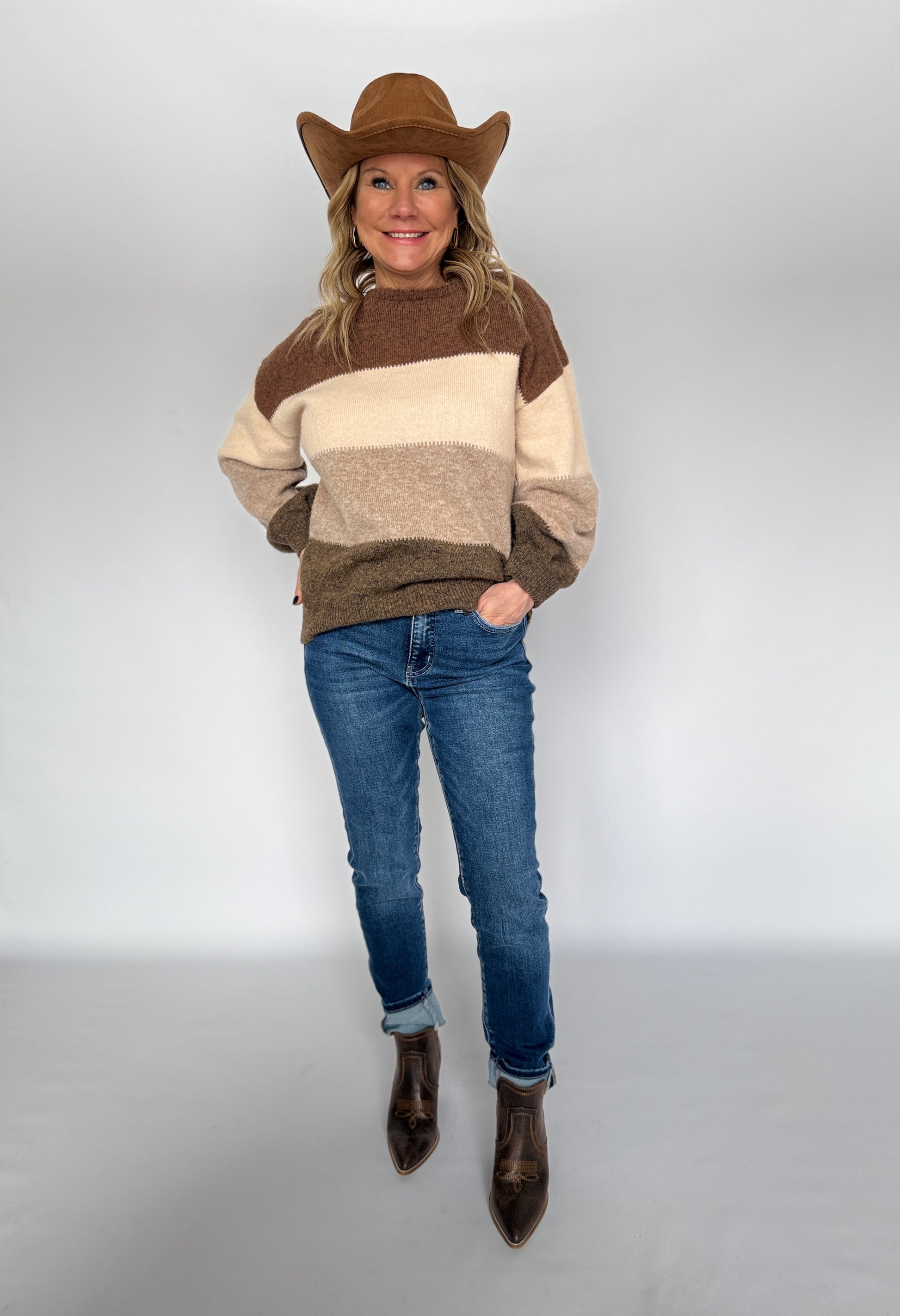Person wearing a brown and beige striped sweater, blue jeans, and a cowboy hat on a white background