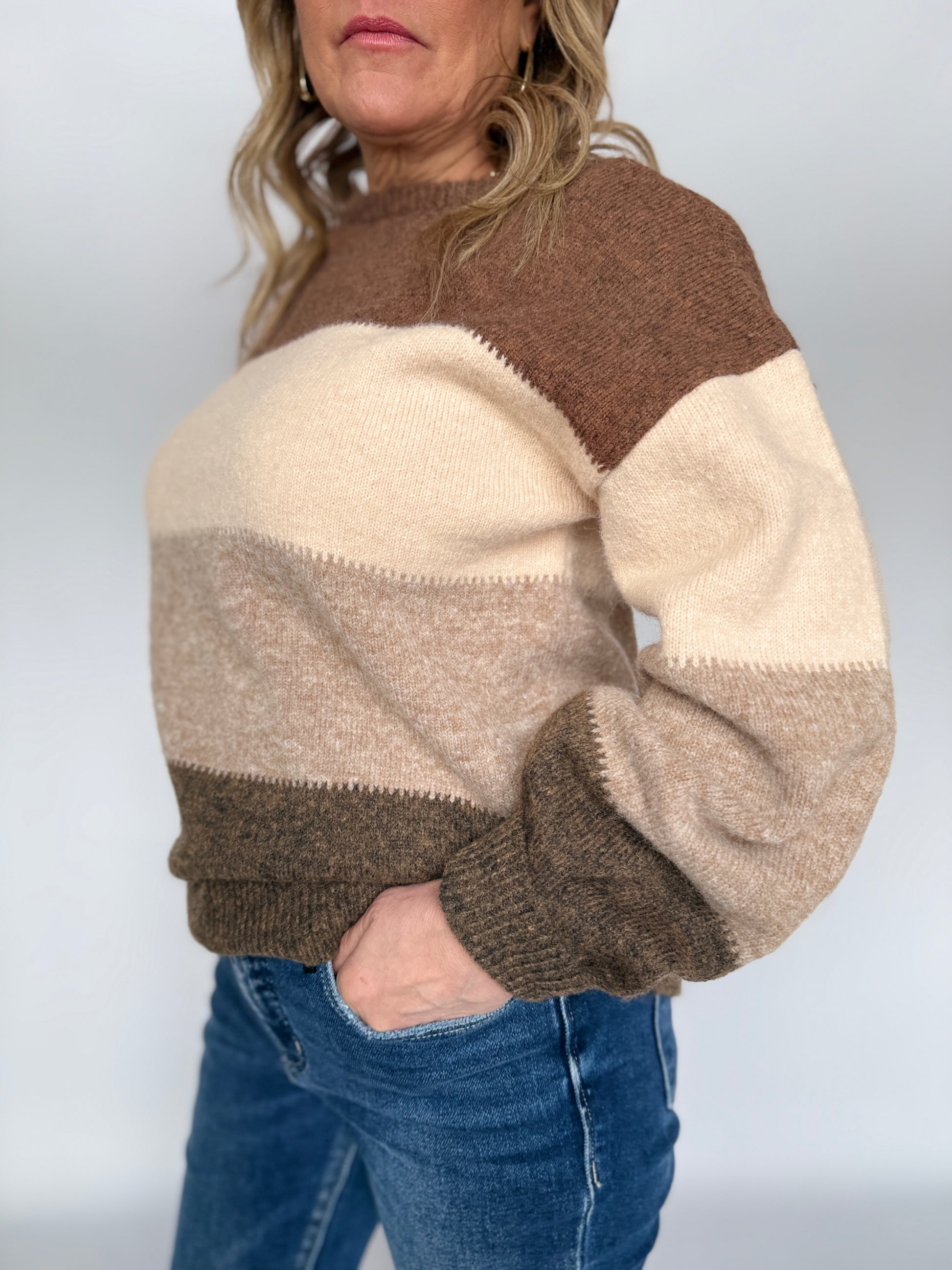 Person wearing a brown and beige color-blocked sweater with blue jeans on a plain background