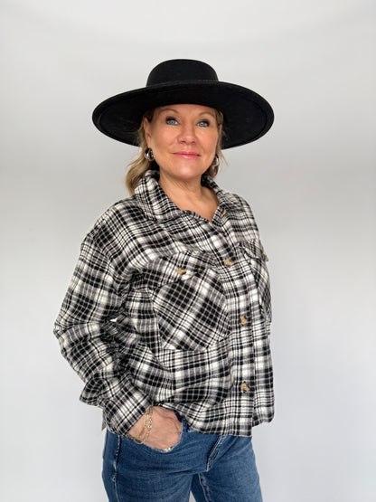 Person wearing a black and white plaid shirt, blue jeans, and a black hat on a plain background