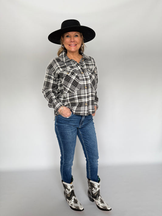 Person wearing a plaid shirt, jeans, and cowboy boots with a black hat on a white background