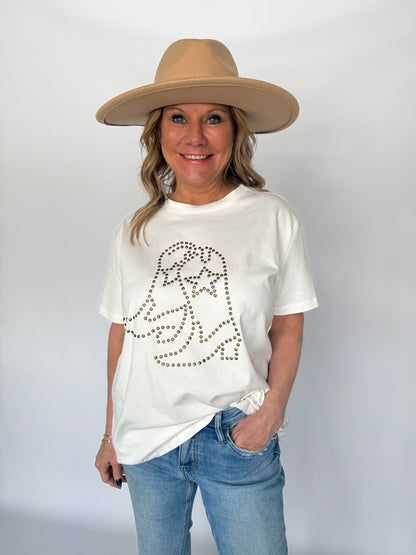 Person wearing a white t-shirt with a graphic design, blue jeans, and a beige hat on a plain background