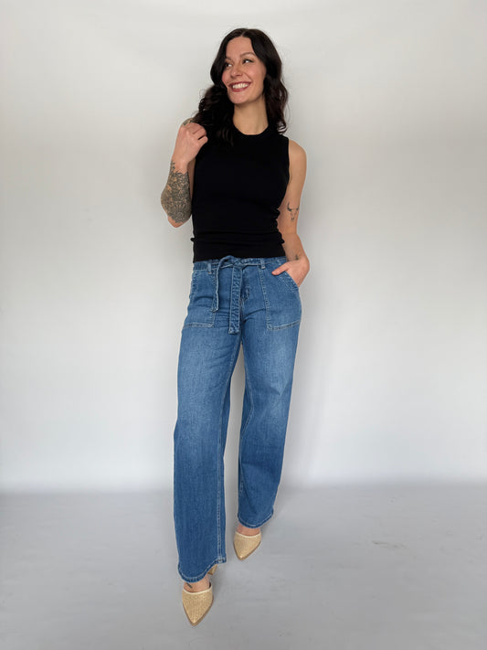 Woman wearing blue jeans and a black top against a white background