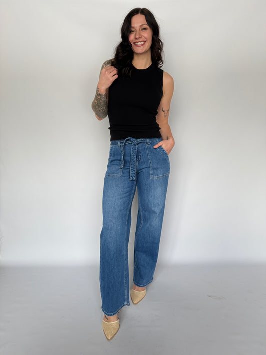 Woman wearing blue jeans and a black top against a white background