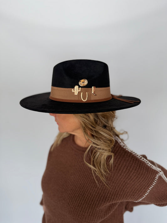 Person wearing a black hat with a brown band featuring gold accents on a plain background