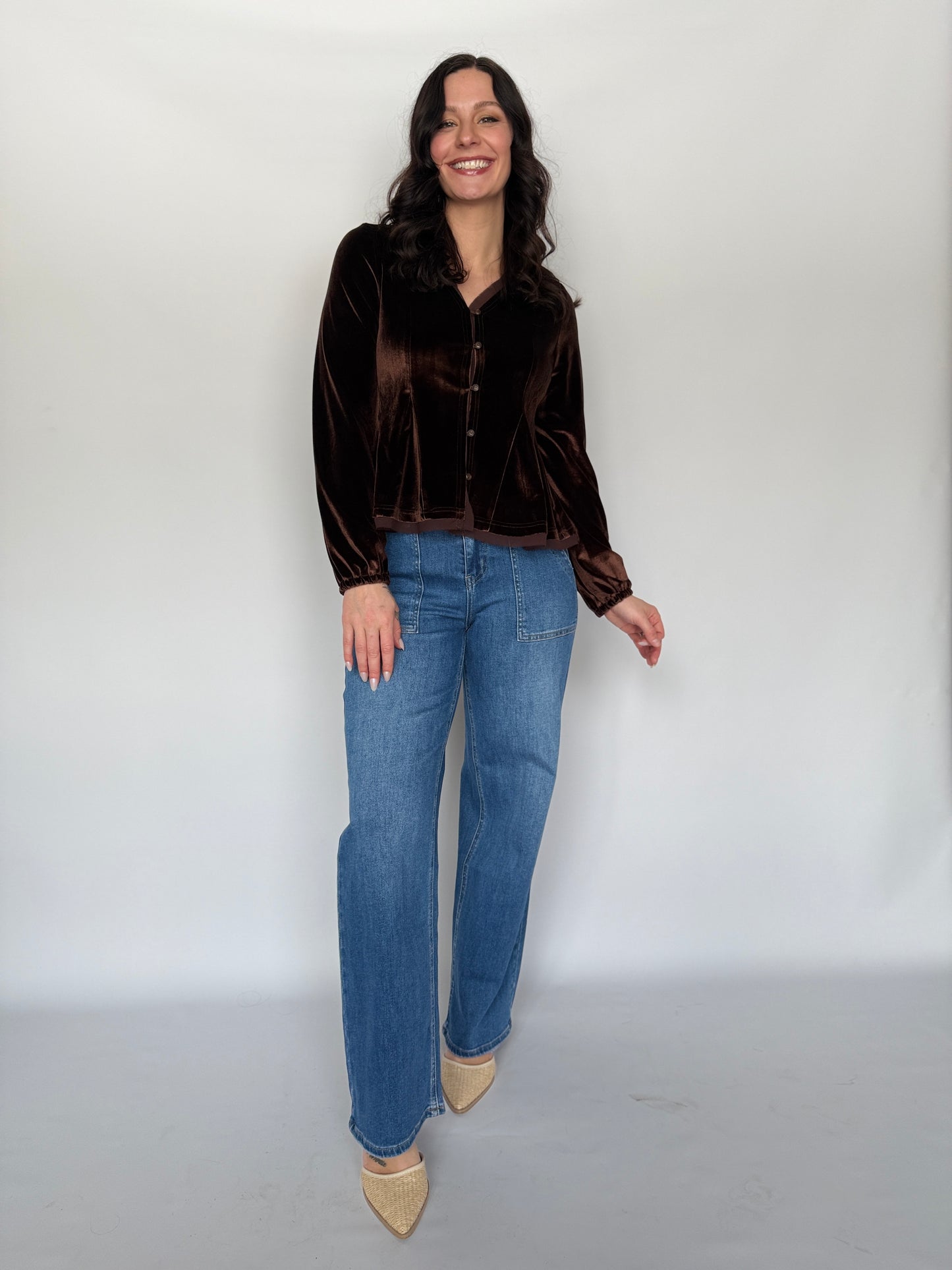 Woman wearing a brown velvet shirt and blue jeans against a white background