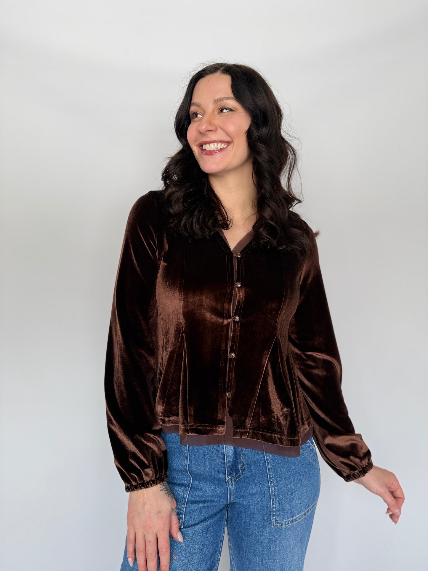 Woman wearing a brown velvet jacket and blue jeans against a white background