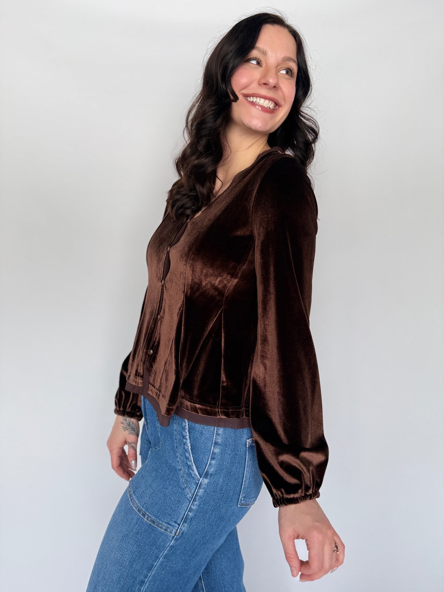 Woman wearing a brown velvet jacket and blue jeans against a white background