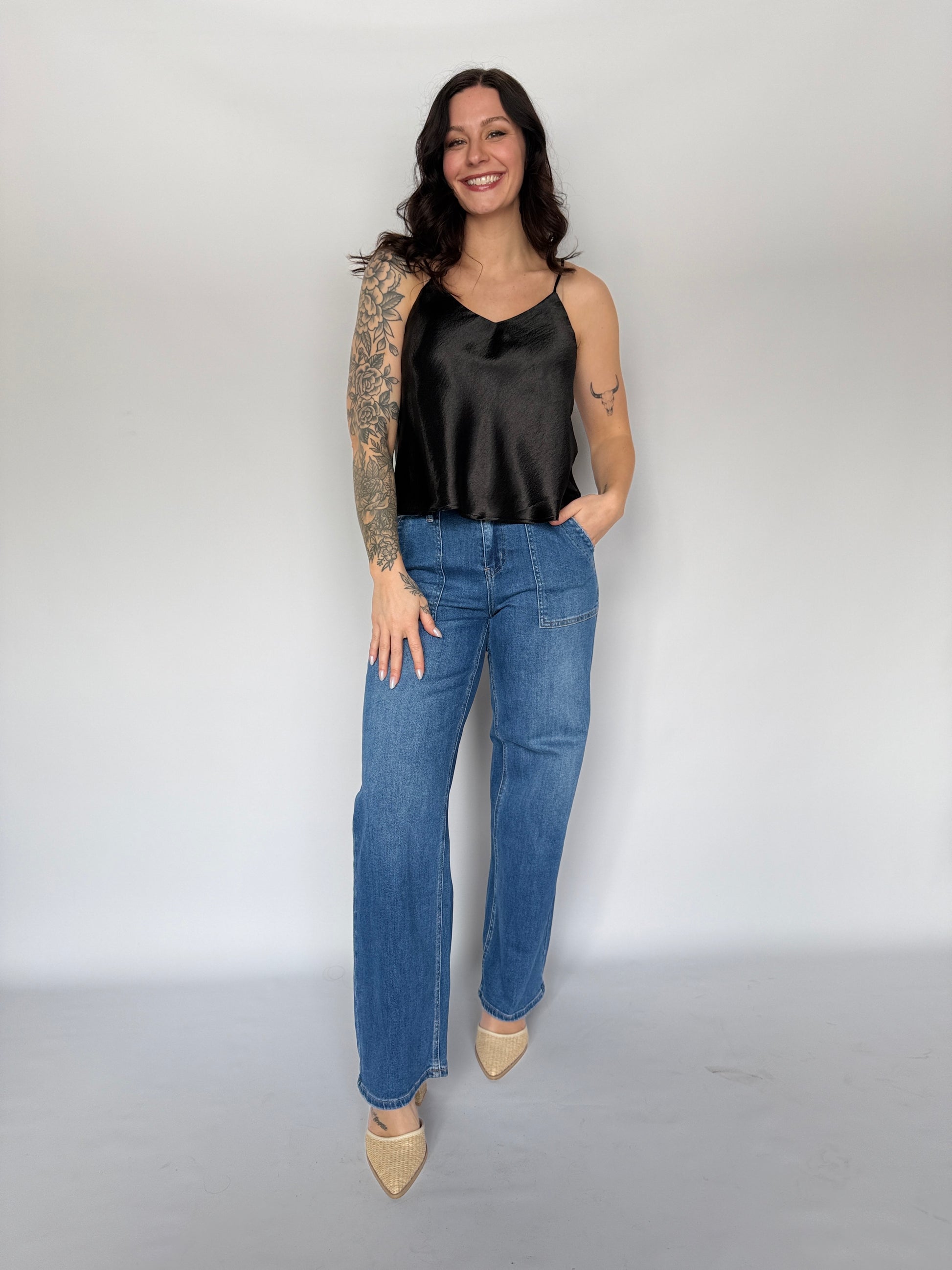 Woman wearing a black top and blue jeans against a white background