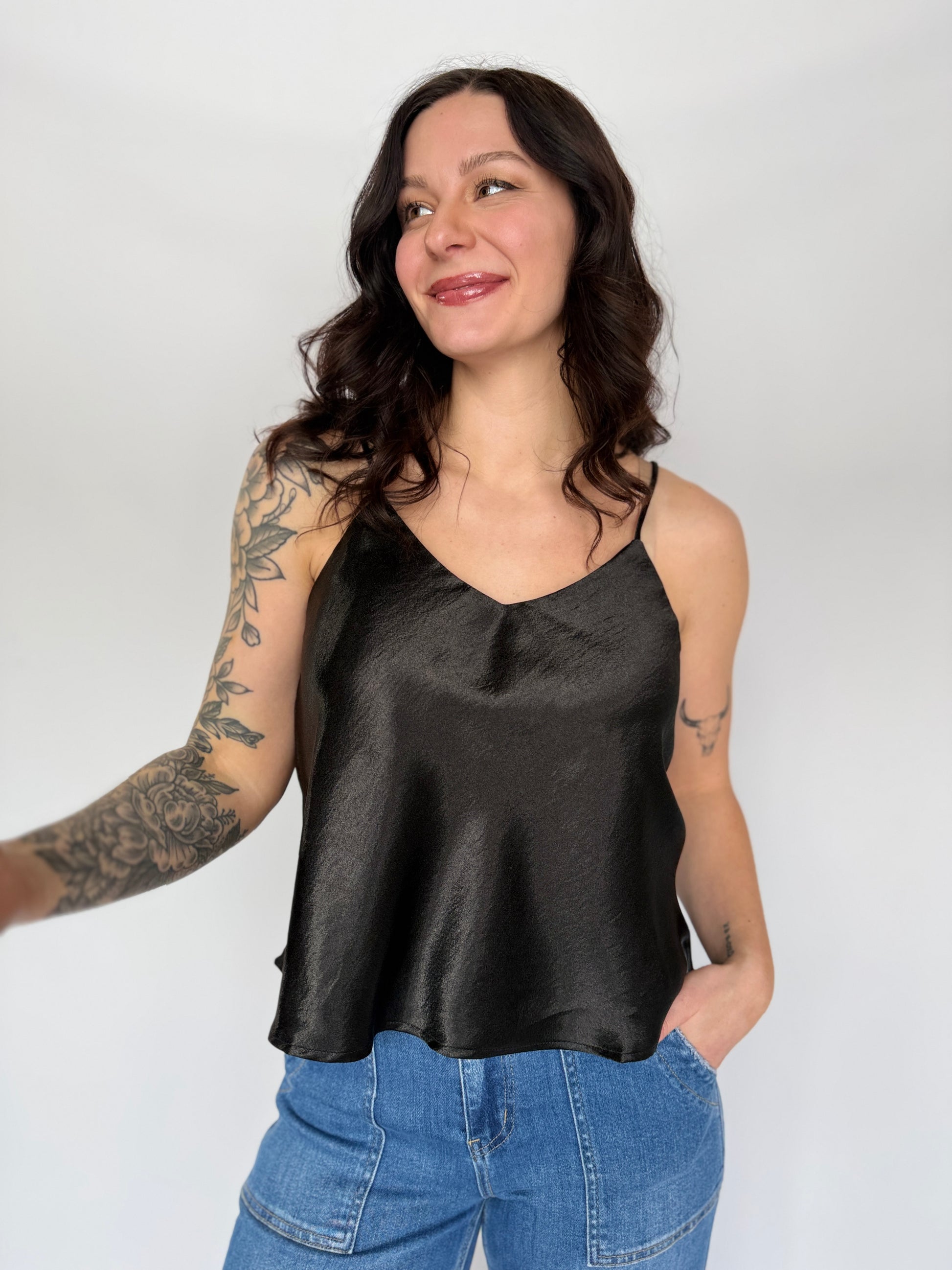 Woman wearing a black satin tank top and blue jeans against a white background