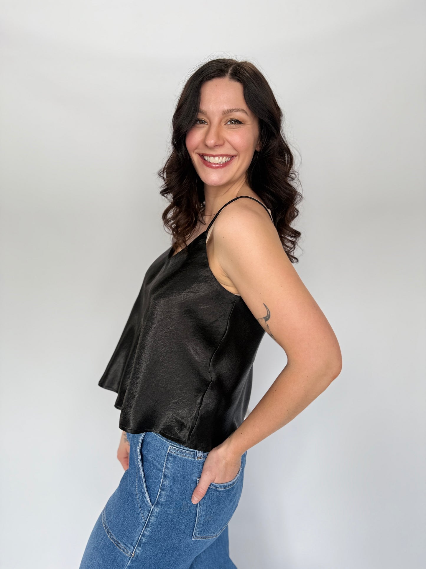 Woman wearing a black satin top and blue jeans against a white background